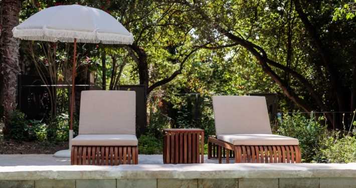 Bains de soleil en bois et parasol à franges au bord de la piscine, parc de La Villa Kara — Drôme