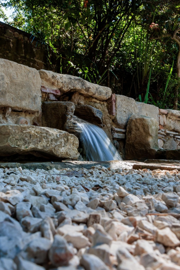 Petite cascade en pierre se déversant sur des graviers blancs, détail du jardin de l'hôtel Drôme La Villa Kara