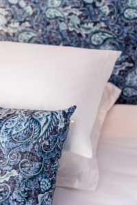 Coussin à motif bleu paisley et linge de lit blanc, détail de literie raffinée à l'hôtel de charme La Villa Kara