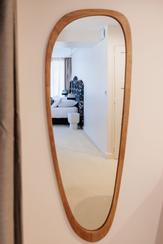 Miroir en bois aux formes organiques reflétant une chambre fleurie, détail déco de l'hôtel La Villa Kara